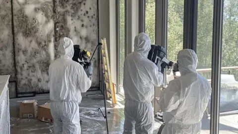 Three crew members in protective suits documenting a mold affected room
