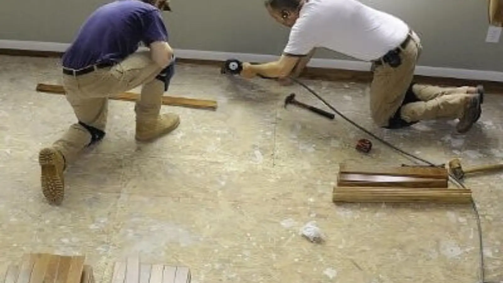 Two contractors on their knees installing new subfloor after water damage